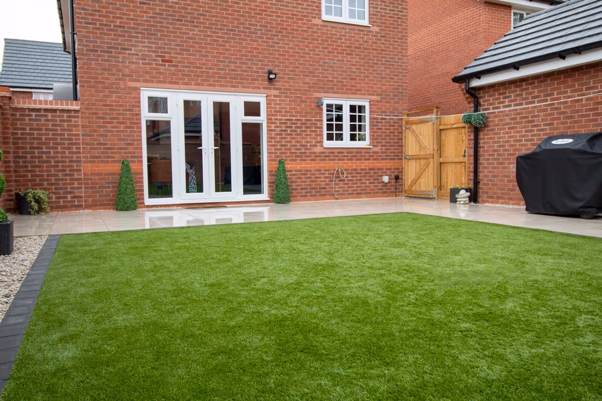 Town Soft Grey, 600x600 Porcelain Slabs with a resin-based jointing compound. A large Charcoal Pencil Edge paver around the perimeters. 35mm Hanbury Artificial Turf. Cotswold 20mm Decorative Chipping stones.