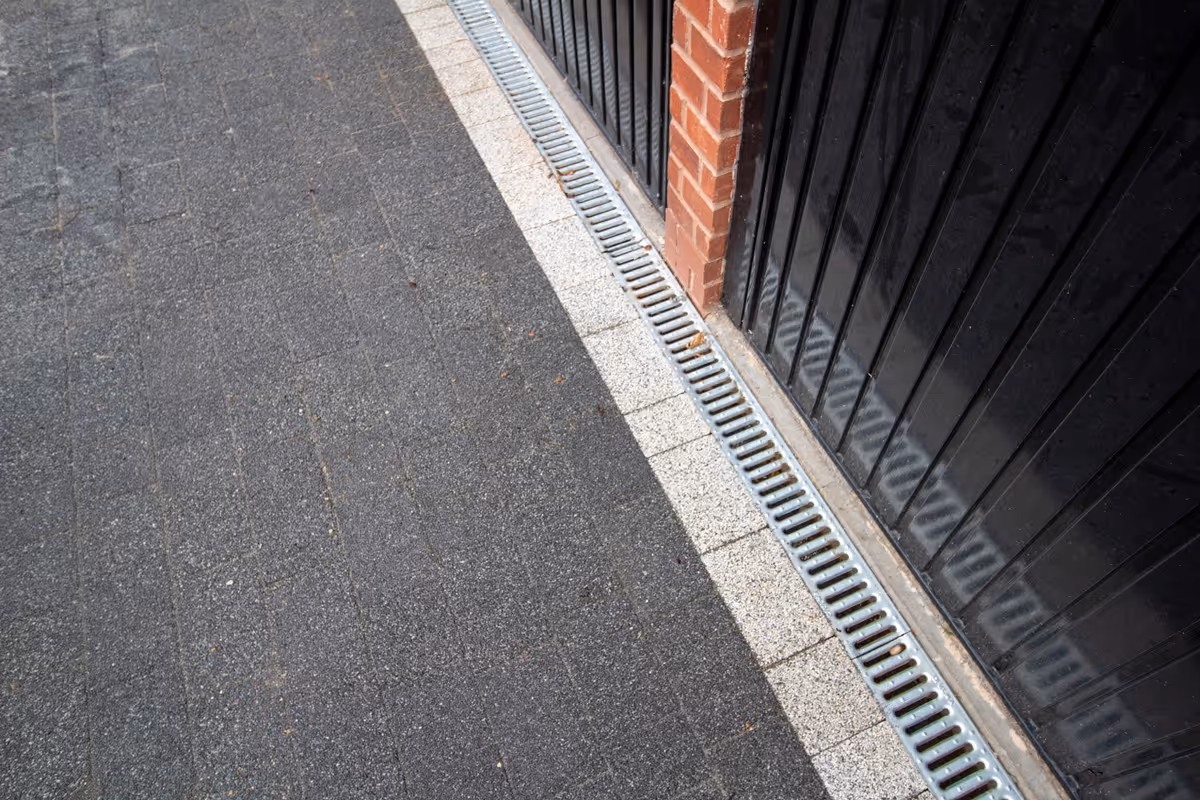 Resin-topped regular block paving driveway with white block border and security posts for a caravan. Retaining wall with tile crease and blue engineering header course - angle 5