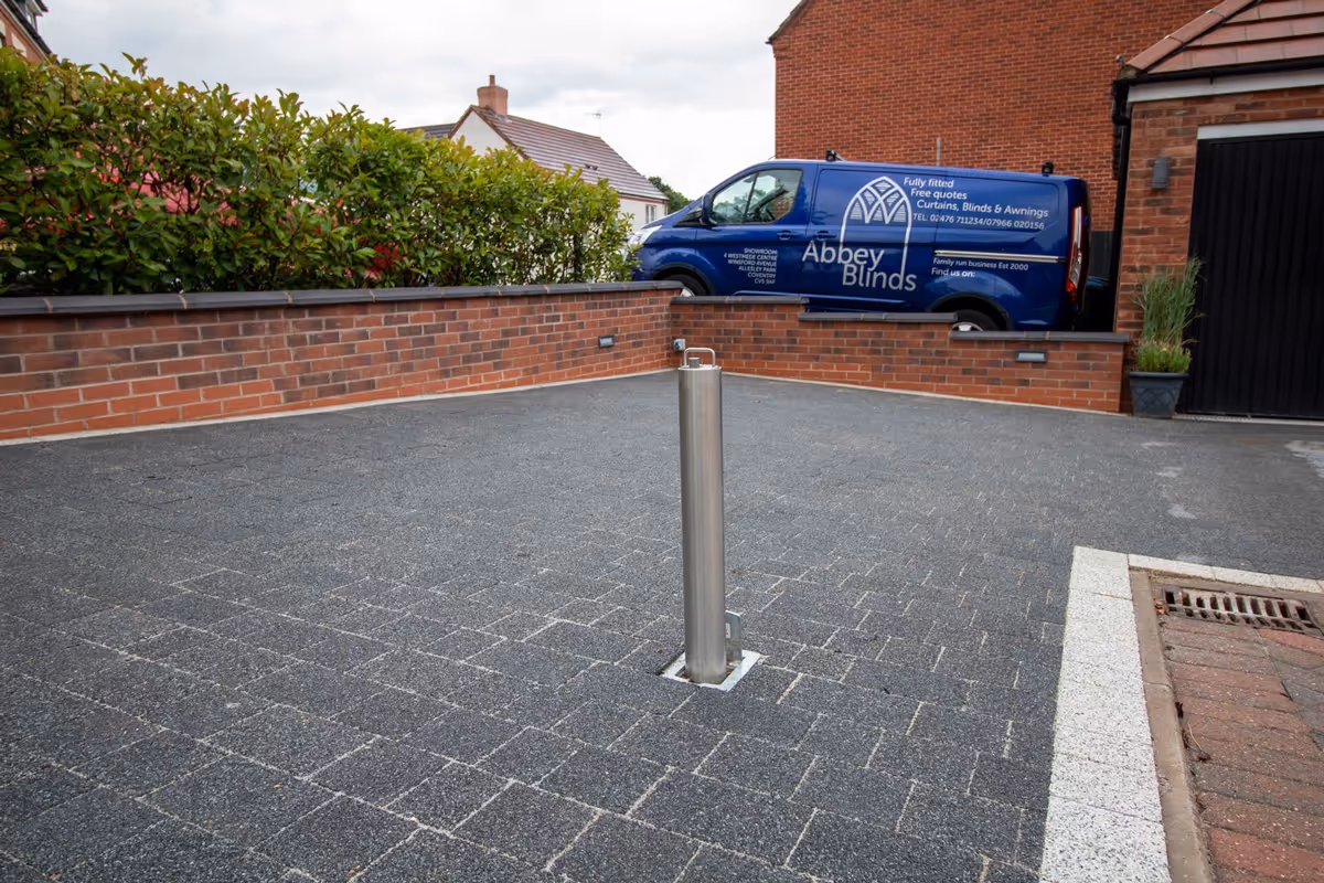 Resin-topped regular block paving driveway with white block border and security posts for a caravan. Retaining wall with tile crease and blue engineering header course - angle 7