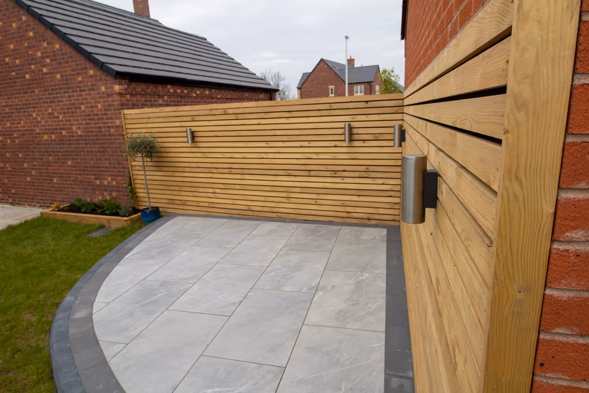 Raised-toped Total Stone Grigio porcelain slabs with Charcoal curb set. Venetian-style screening with downlights. Sleeper beds. Charcoal pencil edge paving border - angle 1