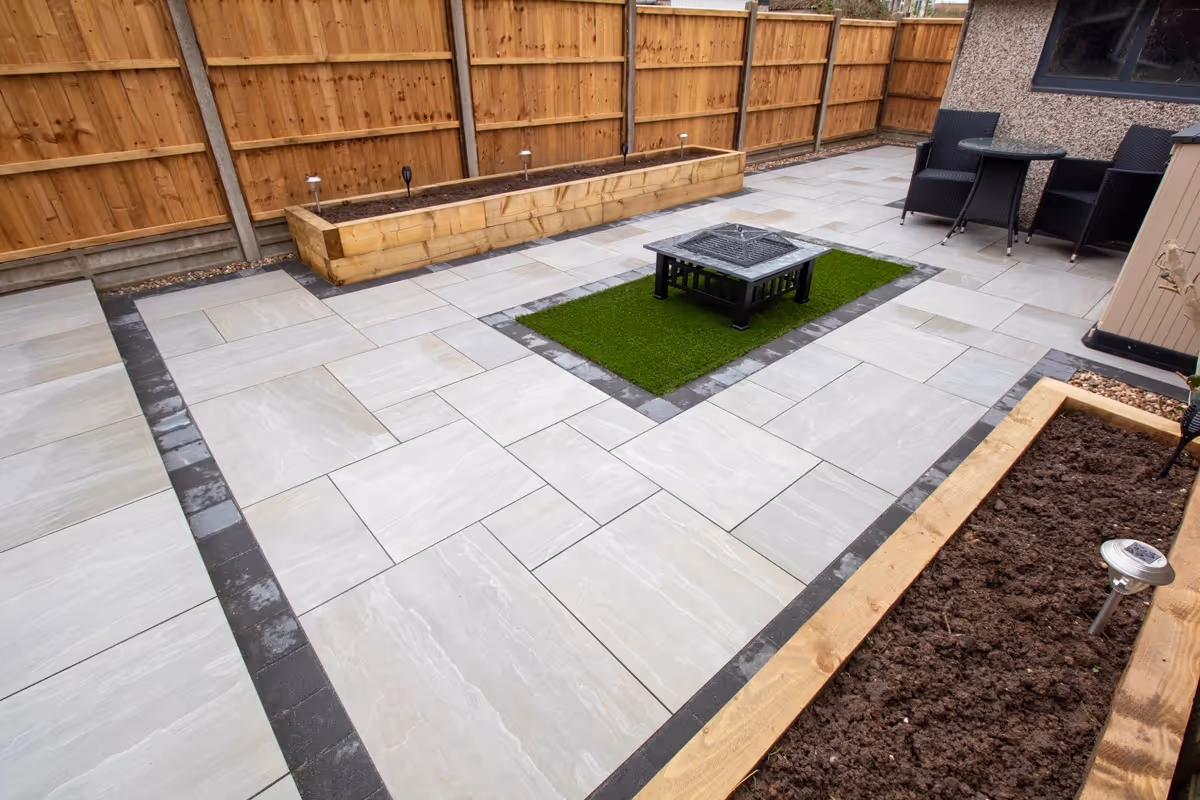 Kandla mixed-size porcelain patio with Charcoal pencil edge paving. Raised sleeper planters. Artificial Turf. New fence and gate - angle 3