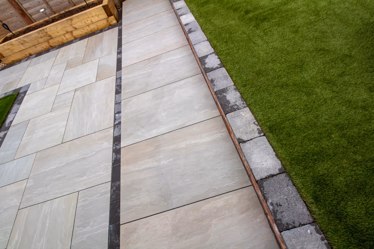 Kandla mixed-size porcelain patio with Charcoal pencil edge paving. Raised sleeper planters. Artificial Turf. New fence and gate - angle 8