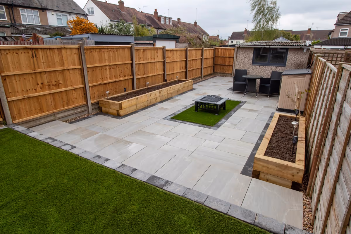 Kandla mixed-size porcelain patio with Charcoal pencil edge paving. Raised sleeper planters. Artificial Turf. New fence and gate - angle 2