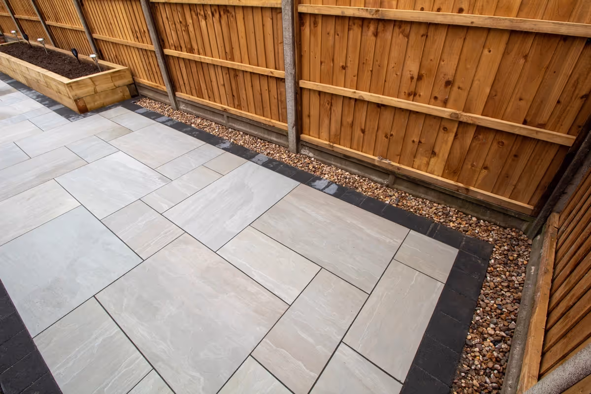 Kandla mixed-size porcelain patio with Charcoal pencil edge paving. Raised sleeper planters. Artificial Turf. New fence and gate - angle 6
