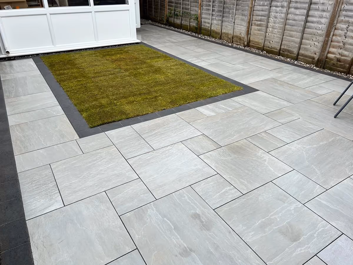 Kandla grey mixed-size porcelain patio with charcoal pencil edge paving. ACO drainage system. Rolawn Medallion turf