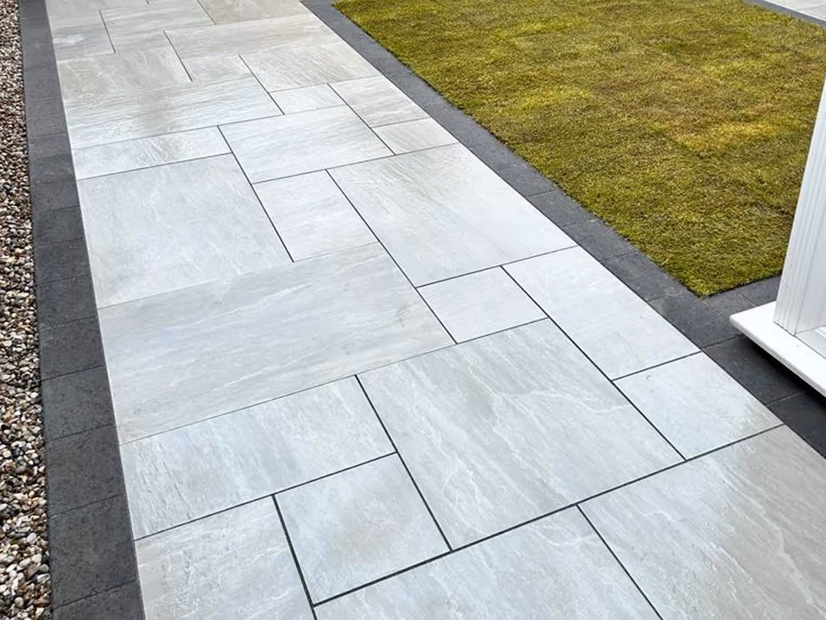 Kandla grey mixed-size porcelain patio with charcoal pencil edge paving. ACO drainage system. Rolawn Medallion turf - angle 1