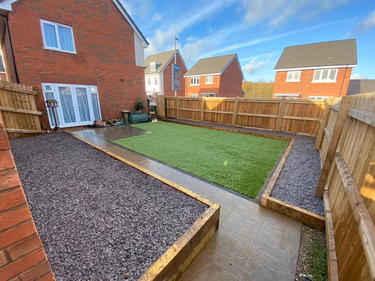 Raised sleeper beds with decorative slate. Extended 450sq riven concrete slabs. Artifical lawn.