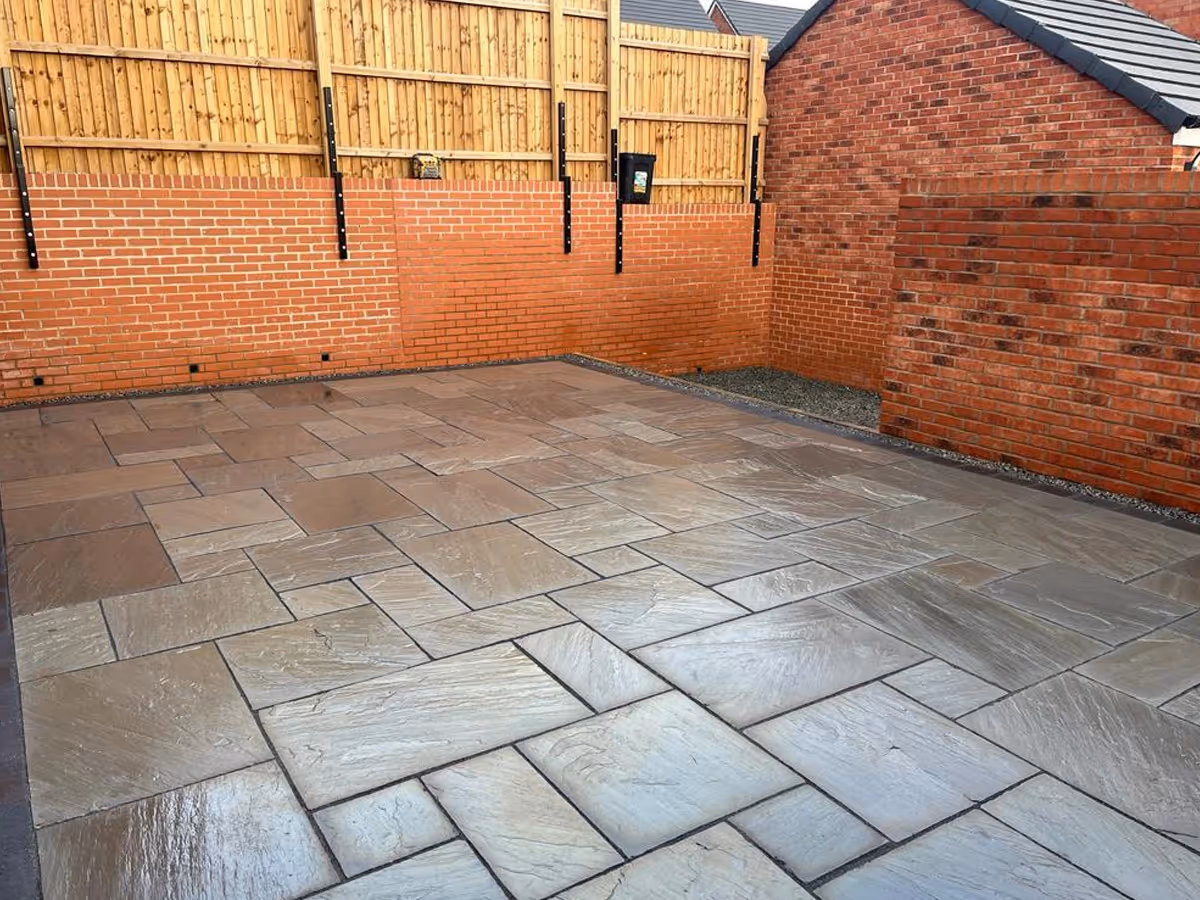 Kandla grey mixed-size Indian natural stone patio with large charcoal aged effect paving. Sleeper retainers. Grey decorative clippings