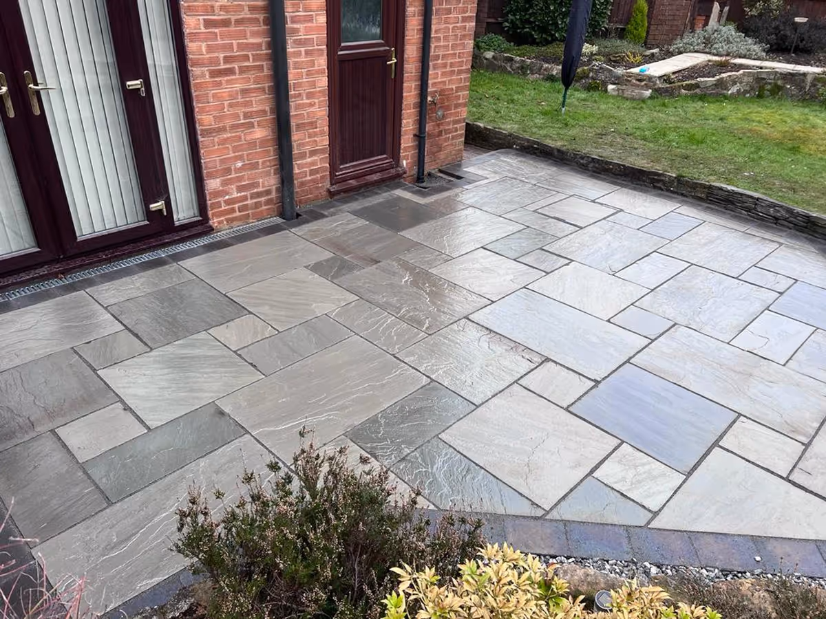 Kandla grey mixed-size Indian natural stone patio with large charcoal aged effect paving. ACO drainage system. Inset manhole tray