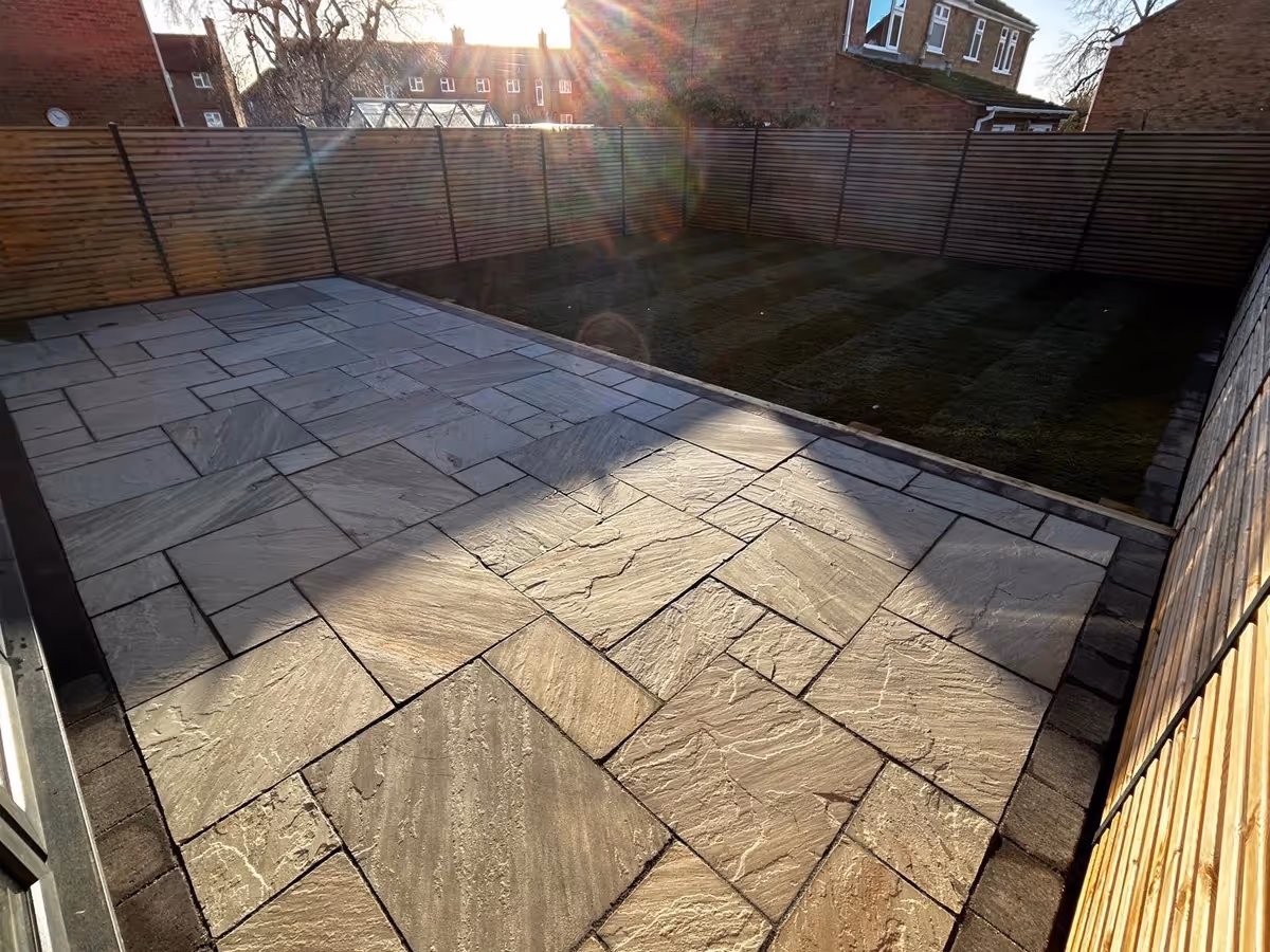 Kandla grey mixed-size Indian natural stone patio with large charcoal aged effect paving. Sleeper retainers. Rolawn Medallion turf.