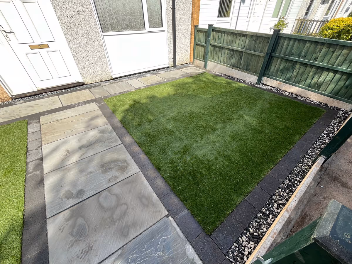 Natural stone patio with charcoal pencil edge paving and artificial lawn