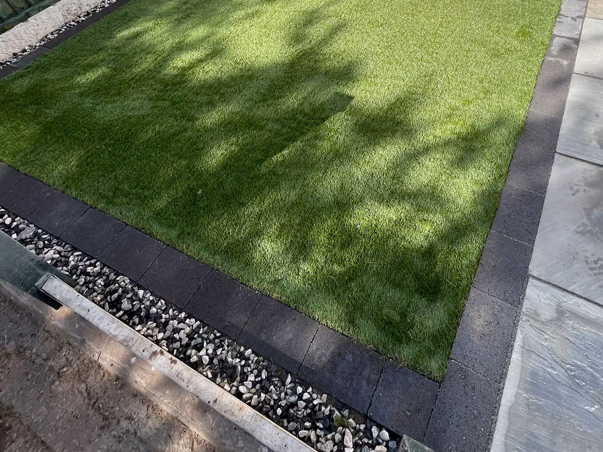 Natural stone patio with charcoal pencil edge paving and artificial lawn - angle 3