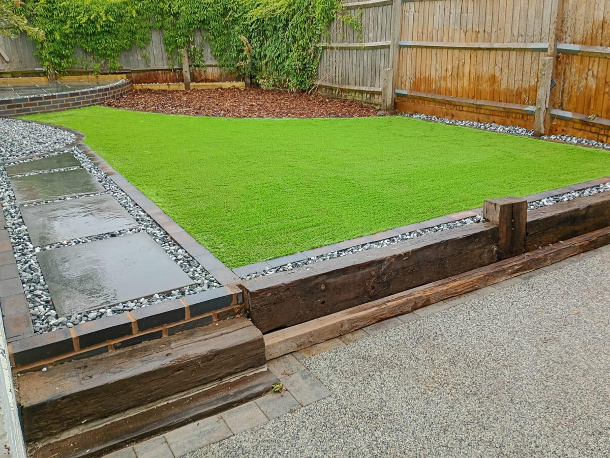 Porcelain patio and pathway with stone surround and paved edges, artificial turf and bark chippings.