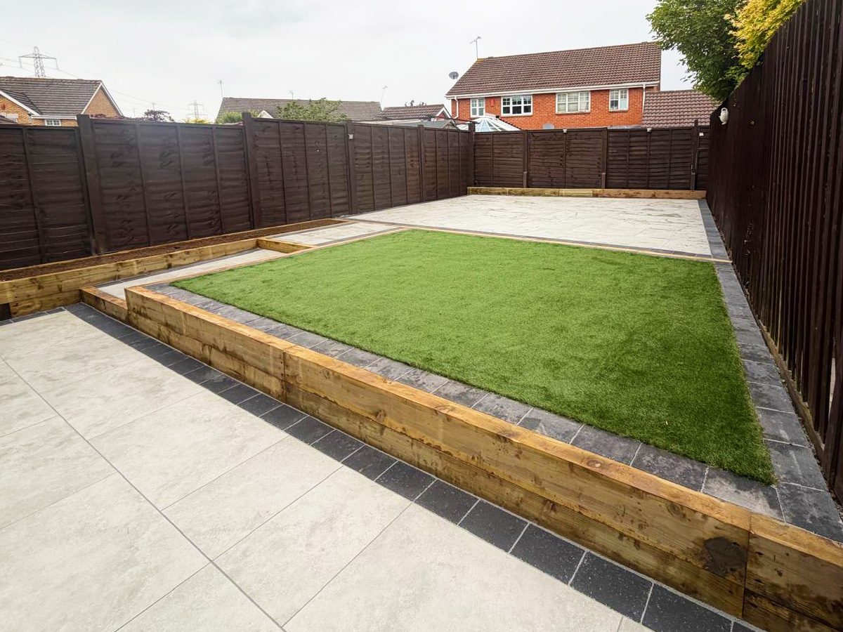 Grey porcelain patio with charcoal pencil edge paving, sleeper retainers and artificial lawn.