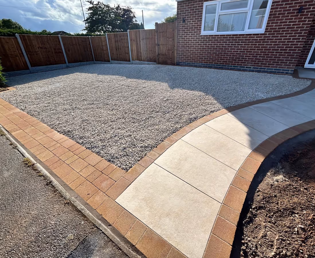 Gravel-covered front yard bordered by brick edging next to a curved concrete walkway beside a brick house.