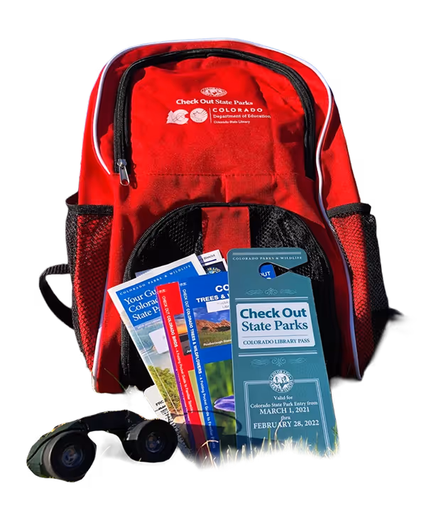 Red family activity backpack with state parks pamphlets binoculars and various outdoor items placed in front of it.