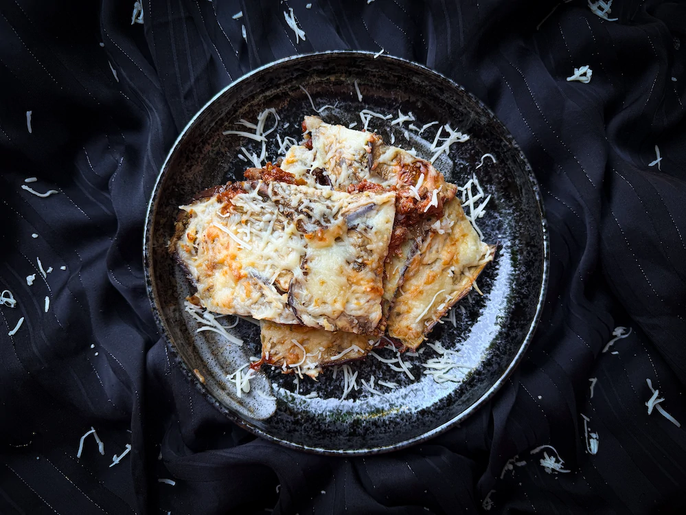 Sur un plat en grès de couleur beige, se trouve la Moussaka avec ses couches alternées de viande et d'aubergine. Avec au dessus le fromage gratiné.
