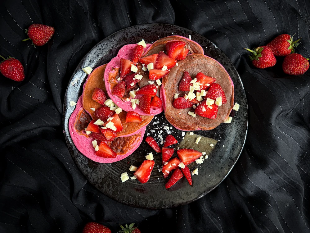 Les pancakes sont empilés au milieux d'une jolie petite assiette noire, les fraises et le chocolat blanc servent de topping.
