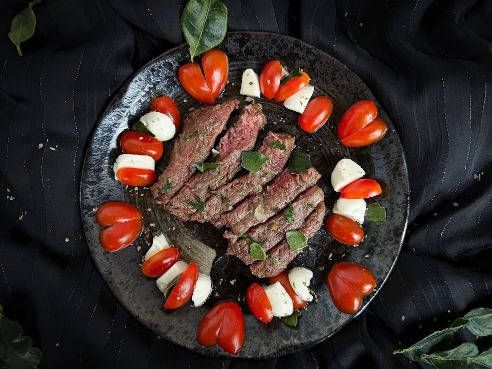 Le filet de boeuf est découpé en tranches au centre de l'assiette décoré de basilic autour se trouvent des tomates cerises et la mozarella.