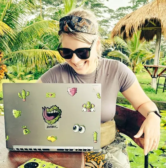 A picture of Disobey Co-founder, Katja Schreiber, sitting at a table surrounded by green smiling at her laptop.