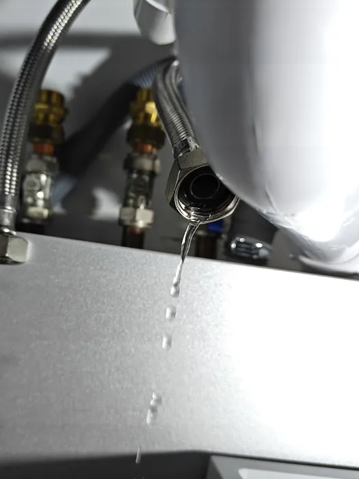 Water dripping from a leaking flexible tap connector under a kitchen sink, drops falling onto the worktop below