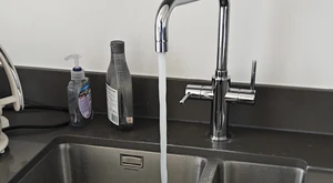 Modern chrome mixer tap running water into a double-bowl kitchen sink after installation