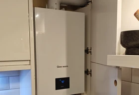 White Glow-worm Compact combi boiler installed in a kitchen cupboard, cabinet door open, digital display reading 70 degrees