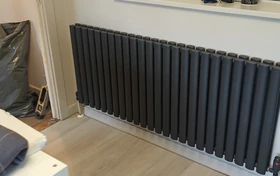 Modern dark grey vertical column radiator on a light wall above wood-effect flooring