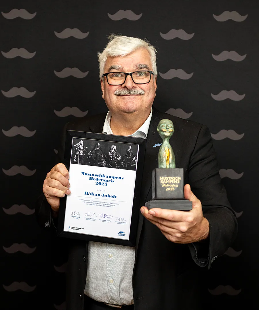 Man med mustasch som håller ett diplom och en skulptur framför sig
