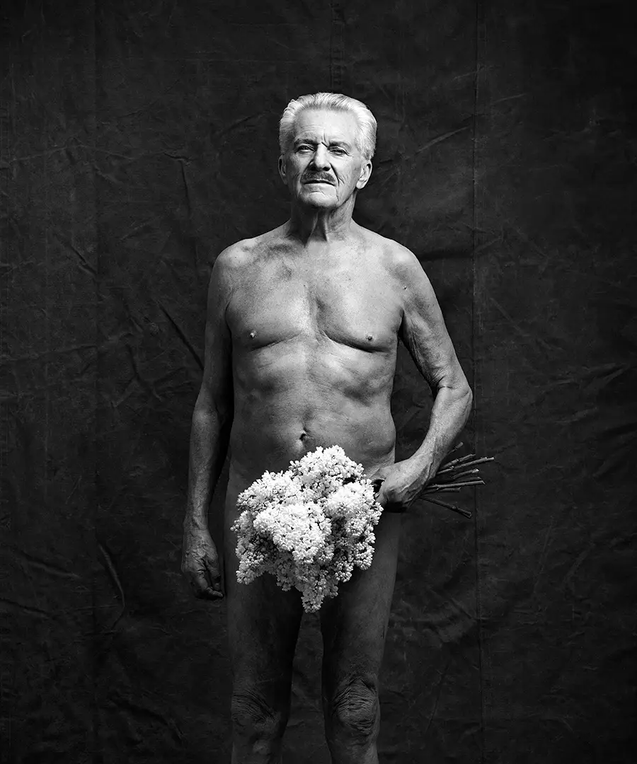 Äldre avklädd man i mustasch som står upp och håller en blombukett i ena handen