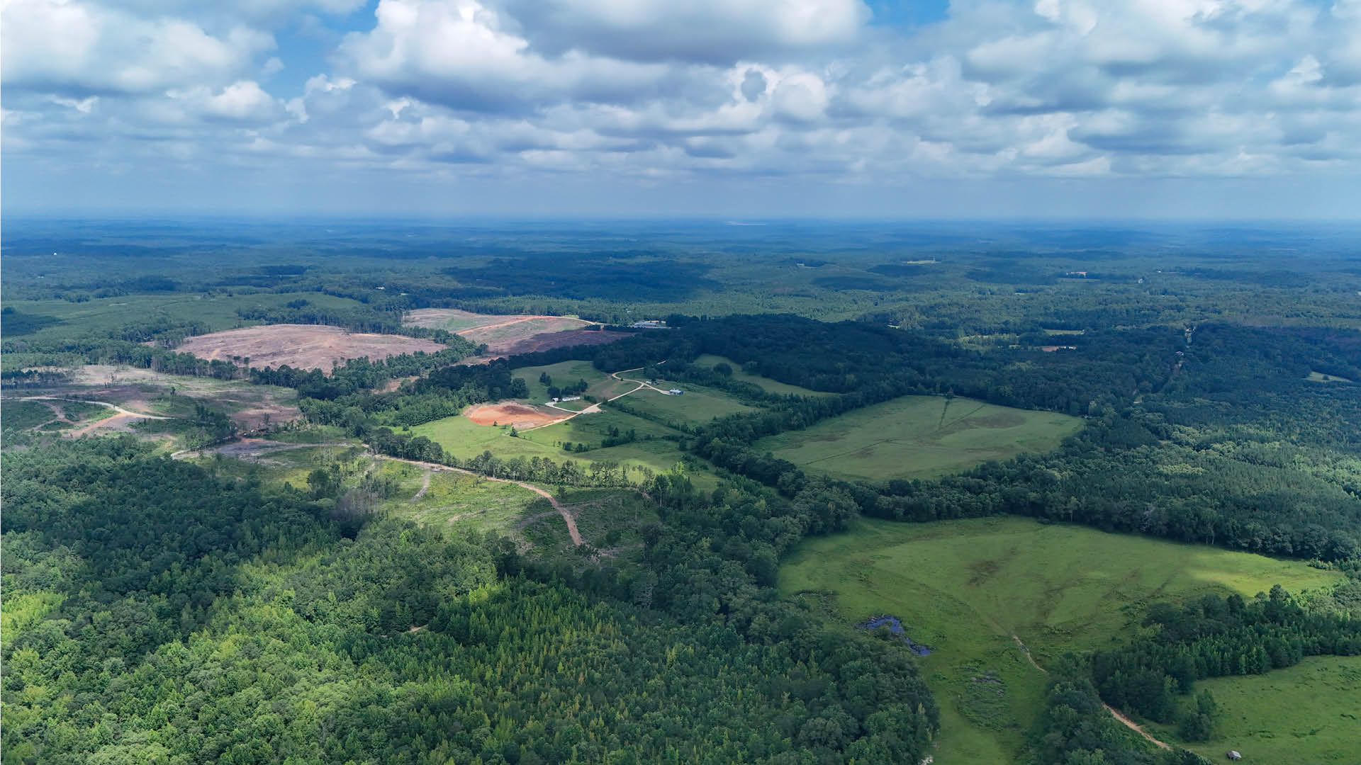 Aerial view of forested land for sale in Choctaw County, Mississippi, featuring a long road through green acreage starting at $15,400.