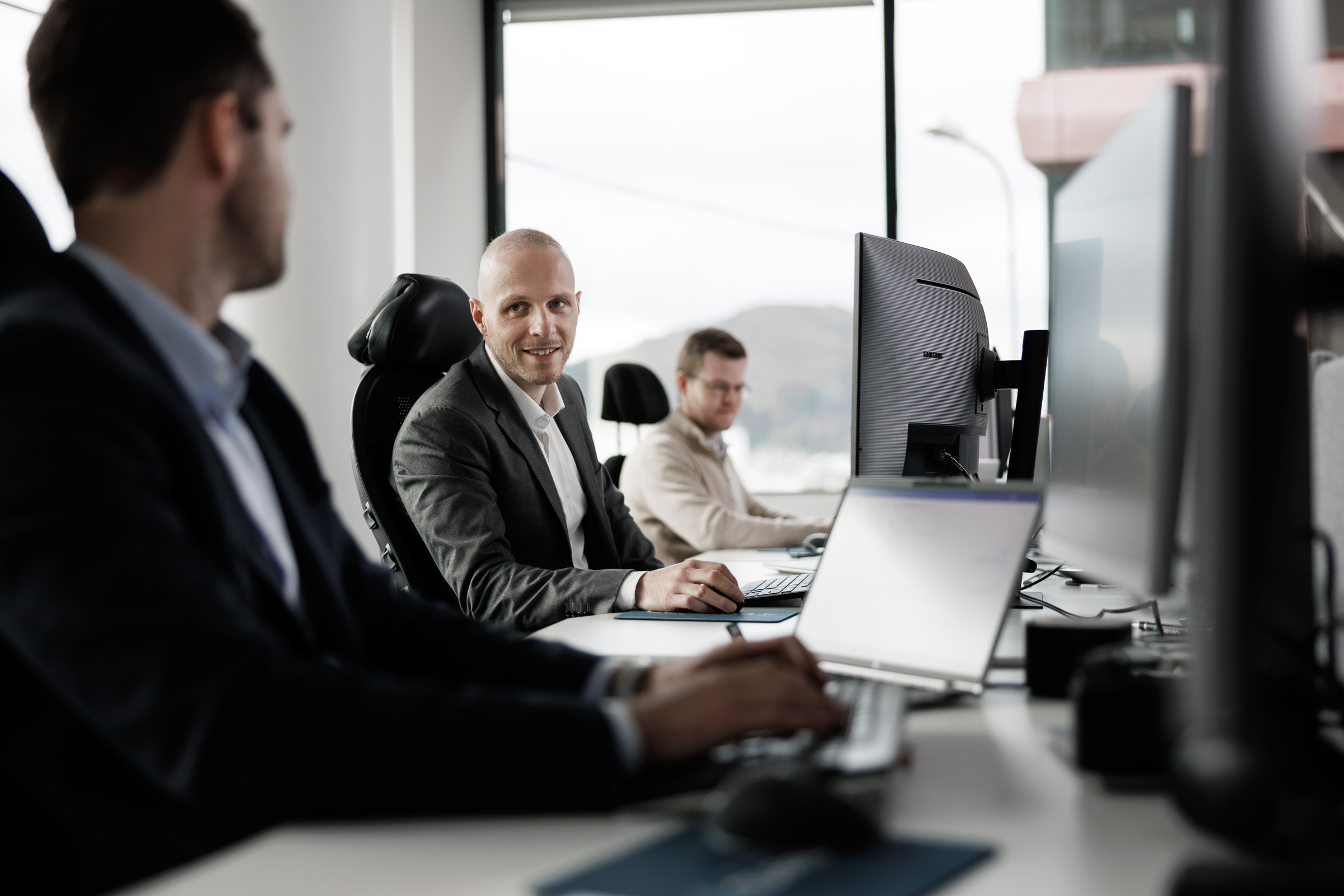 Three men in suits sitting in a meeting, one man in the center smiling and focused.