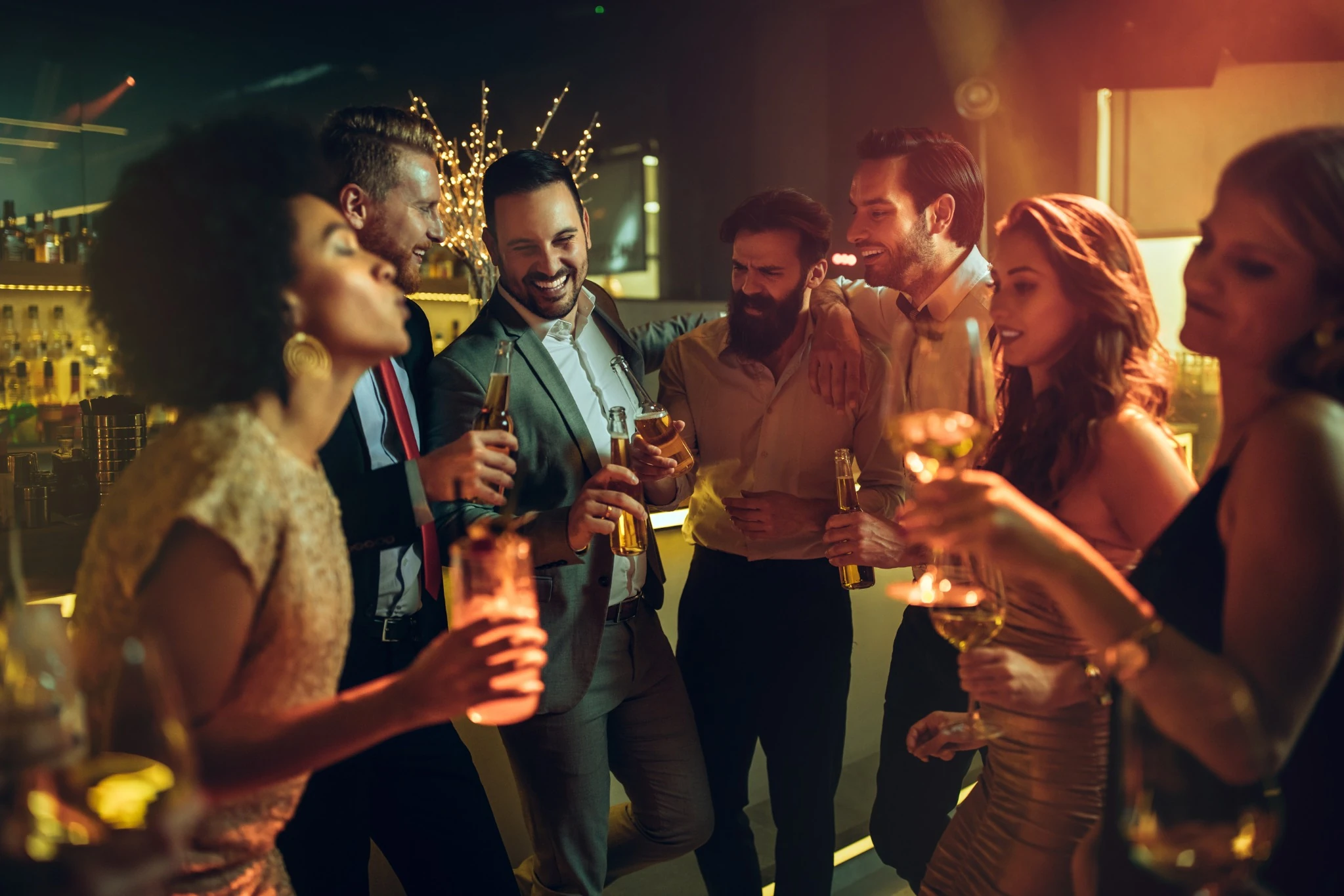 Group of young adults dressed up, holding drinks, enjoying a lively night out at a bar or club.