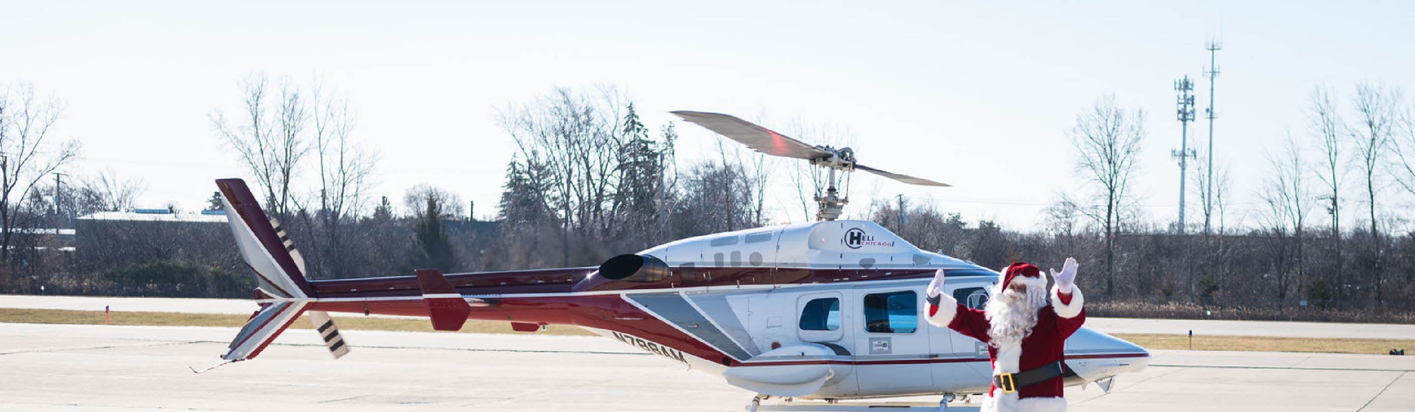 Santa waving beside a helicopter on the landing pad at Schaumburg Regional Airport.