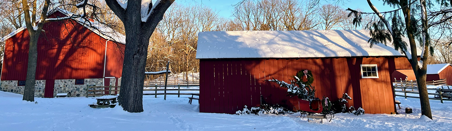 Red barns at Volkening Heritage Farm covered in snow, decorated with a wreath.