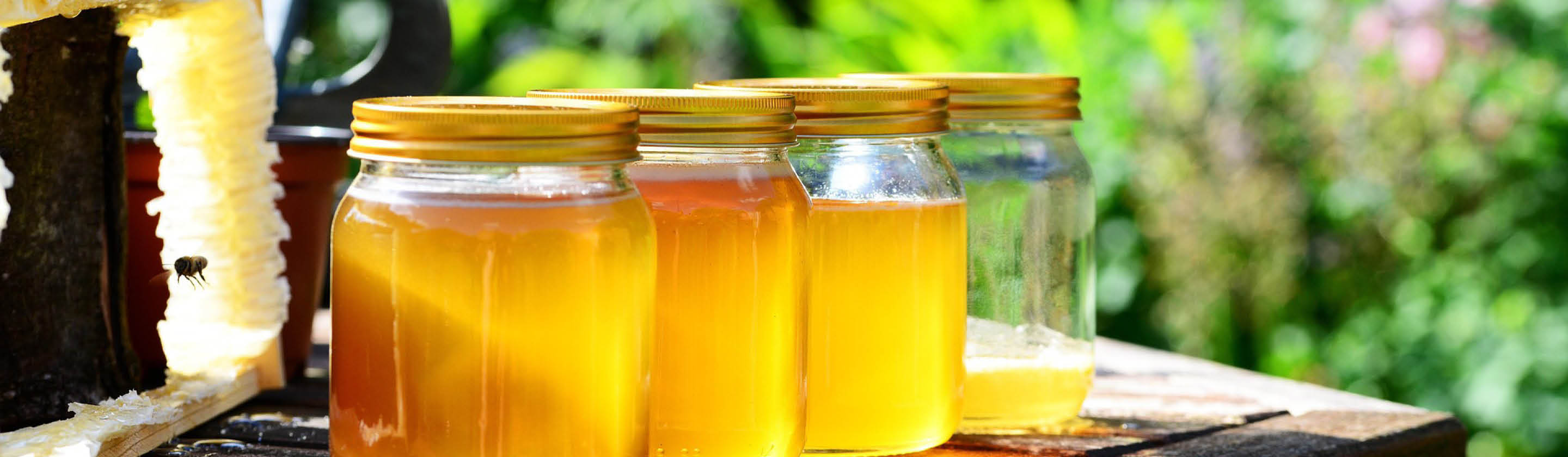 Jars of golden honey beside honeycomb on a wooden table.