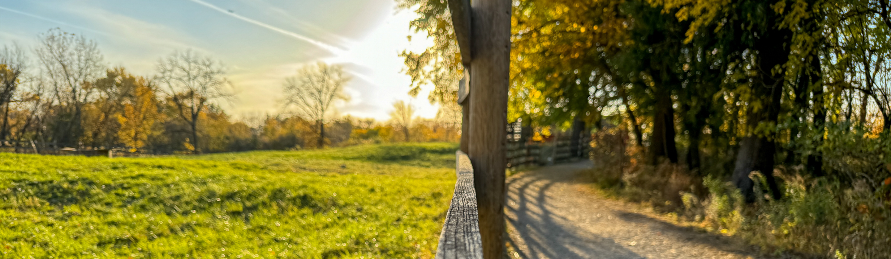 Spring Valley trail beside a wooden fence and meadow in autumn sunlight.