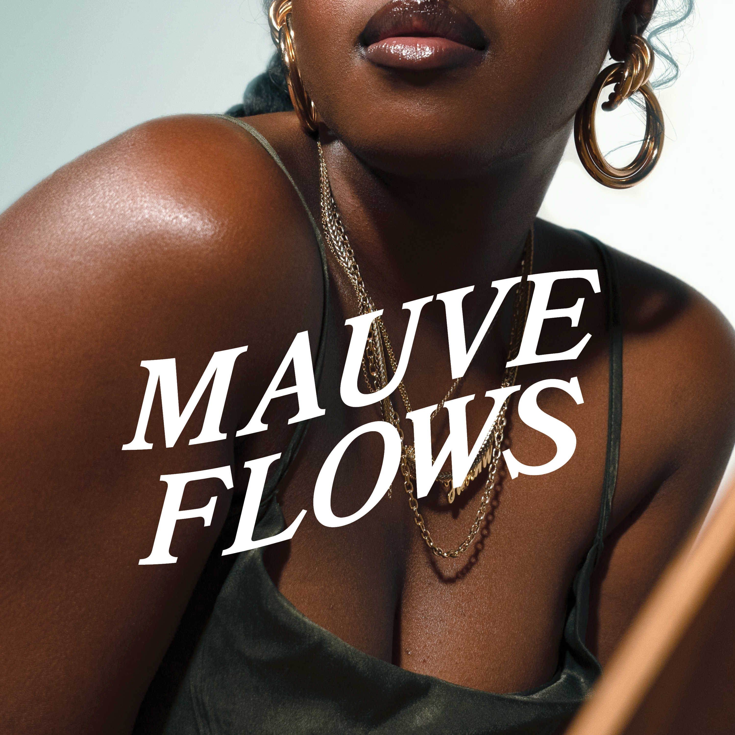 Close-up of a dark-skinned woman wearing gold hoop earrings and layered gold necklaces with the text 'MAUVE FLOWS' over her chest and shoulder.