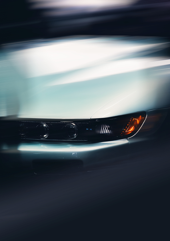 Close-up of a car's front corner featuring headlights and an amber turn signal with motion blur effect.