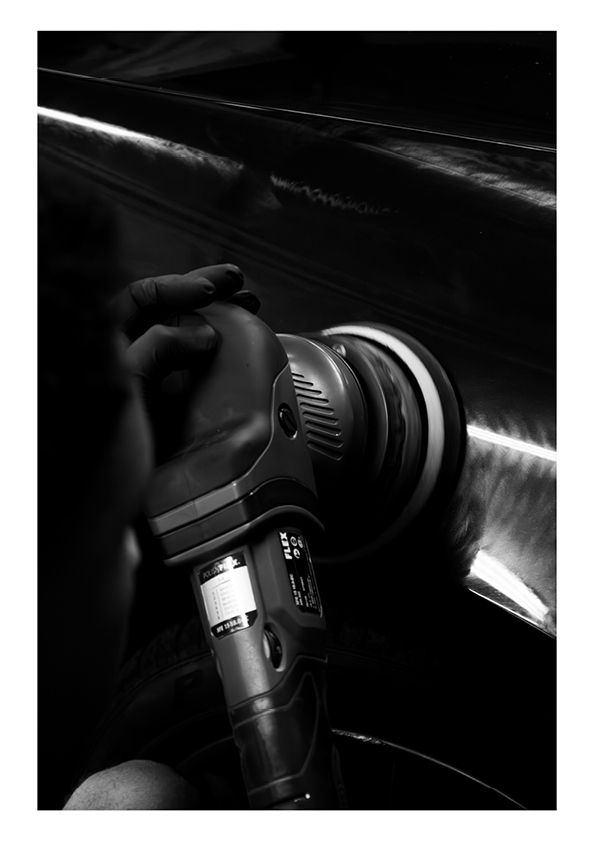 Close-up of a person using an electric buffer to polish the side of a car.