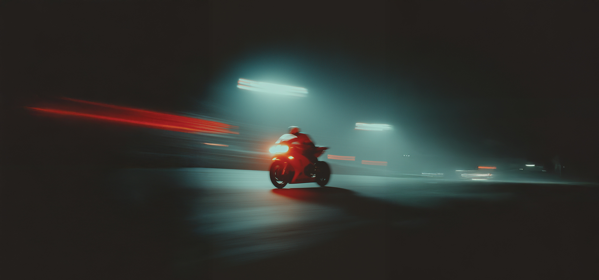 Motorcycle speeding at night with blurred red and white lights and illuminated street lamps.