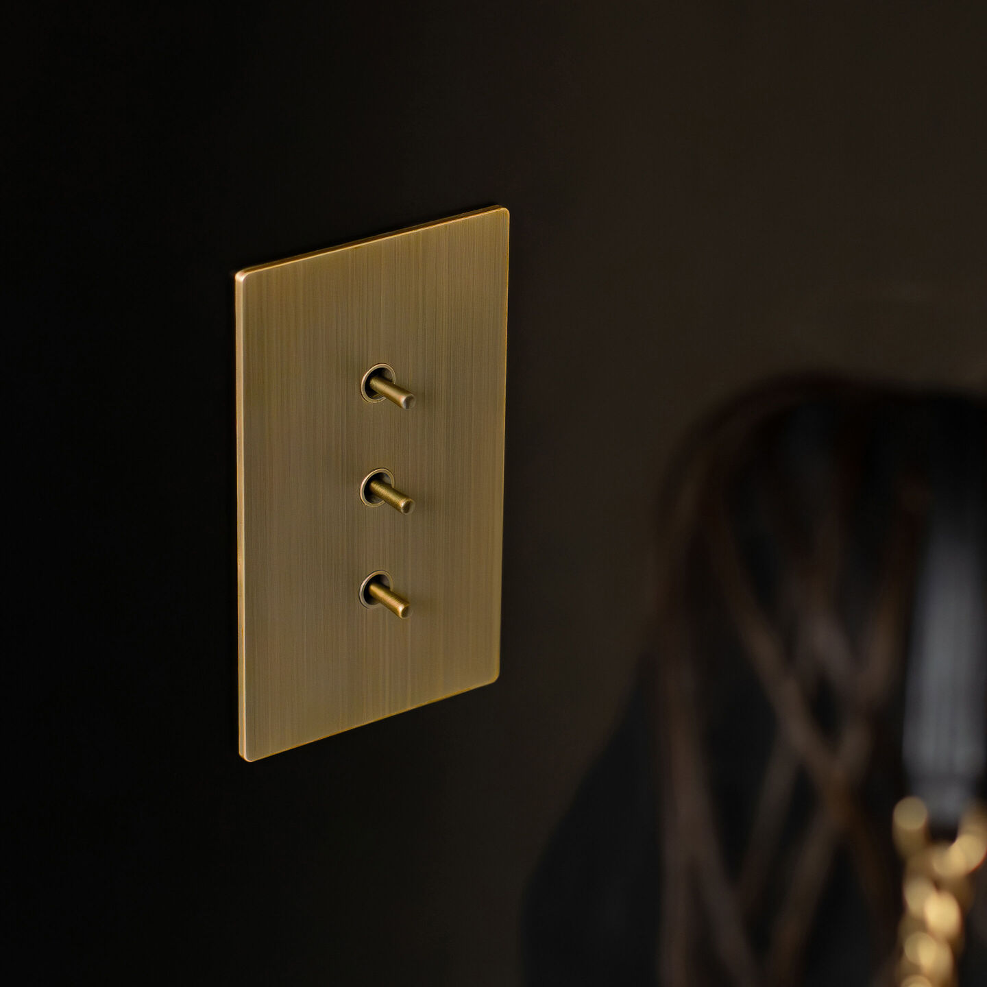 Lutron Aviena three-toggle brass keypad on a dark interior wall