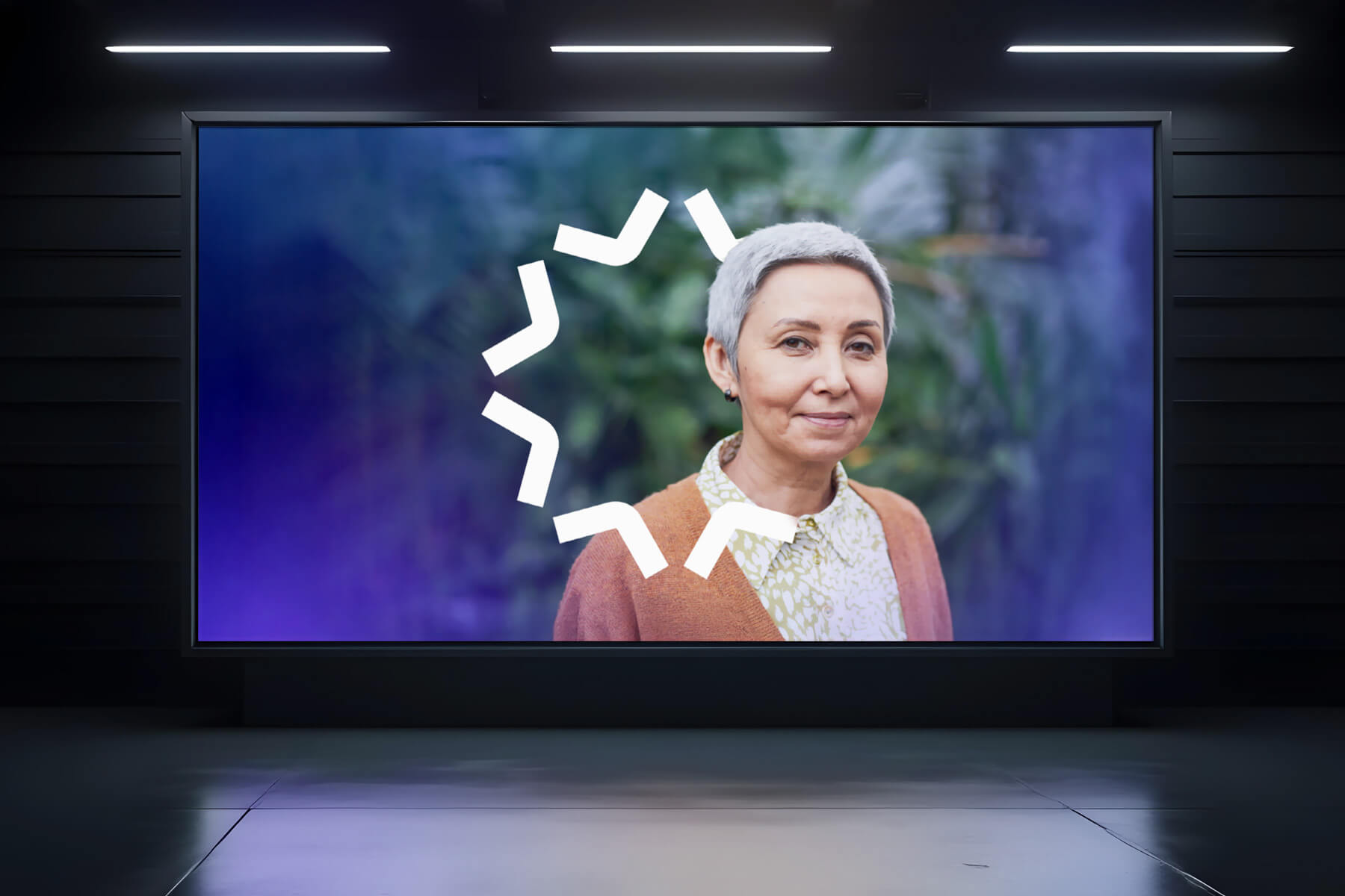 Digital billboard displaying a portrait of a smiling older woman with short gray hair against a blurred green and purple background, with a white circular loading icon overlaid.