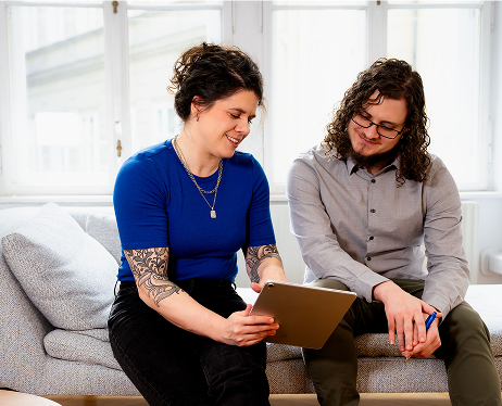 Two people sitting on a sofa, looking at a tablet together.