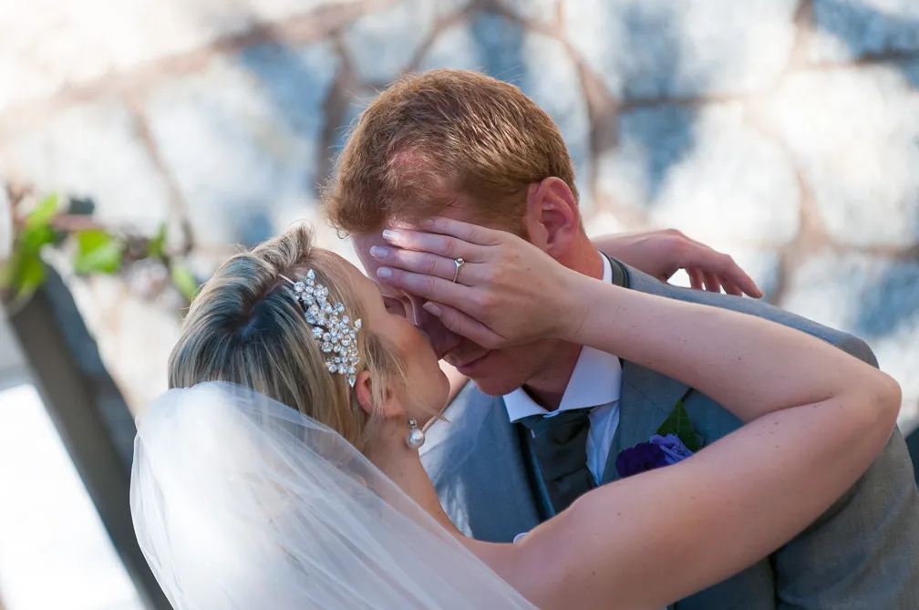Bride covering groom’s eyes with her hand as they lovingly embrace on their wedding day.