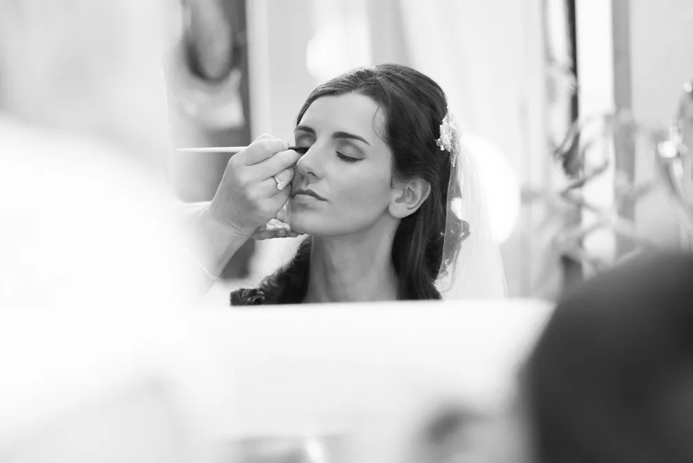 Bride with closed eyes having her makeup applied with a brush before the wedding.