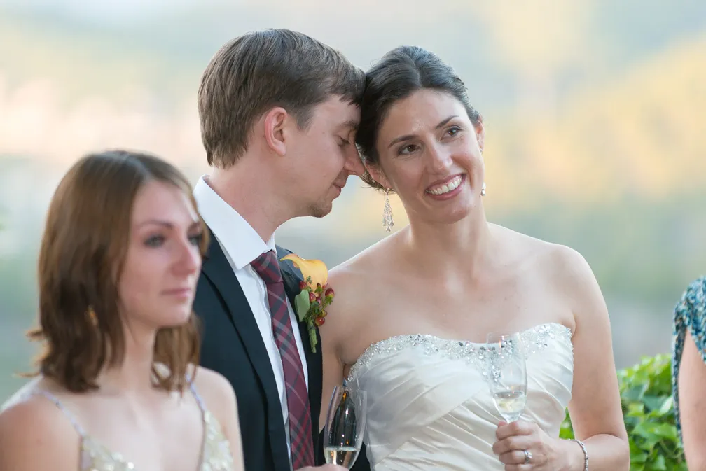 Bride in a white strapless wedding dress smiling with groom in a suit and tie holding champagne glasses.