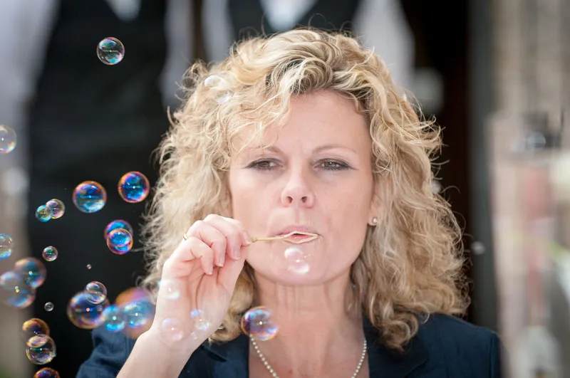 Woman with curly blonde hair blowing bubbles using a small bubble wand.