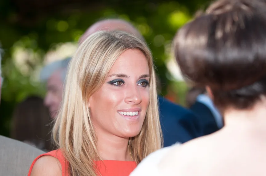 Smiling blonde woman wearing an orange sleeveless top, engaged in conversation with a person whose back is to the camera.