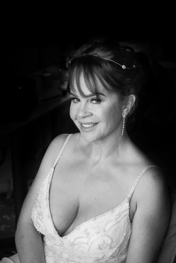 Smiling woman with bangs wearing a delicate headpiece and an embellished sleeveless dress.